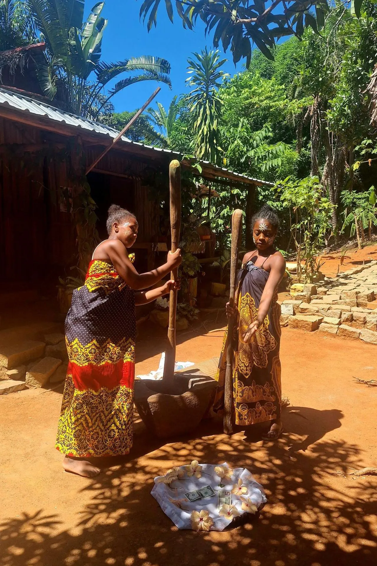 Vrouwen in kleurrijke doeken stampen eten in een houten vijzel in Antsiranana, Madagaskar