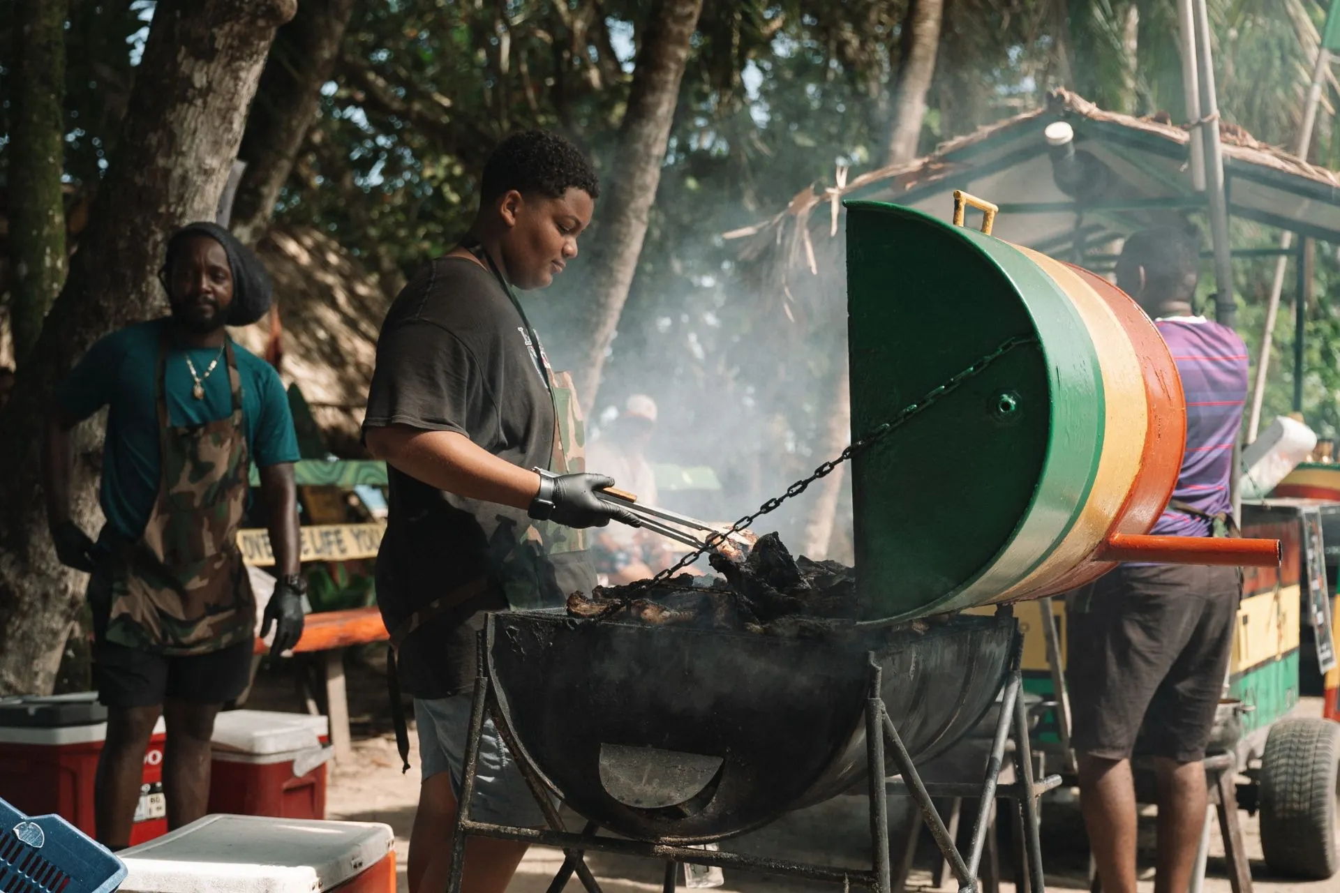 Een barbecue met lokale gerechten in de open lucht, met een kok die het eten bereidt, omgeven door een tropische omgeving.