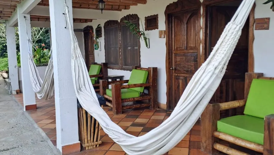 Traditionele veranda met houten deuren en ramen, groene stoelen en twee witte hangmatten, gelegen onder een houten dak met terracotta vloer.