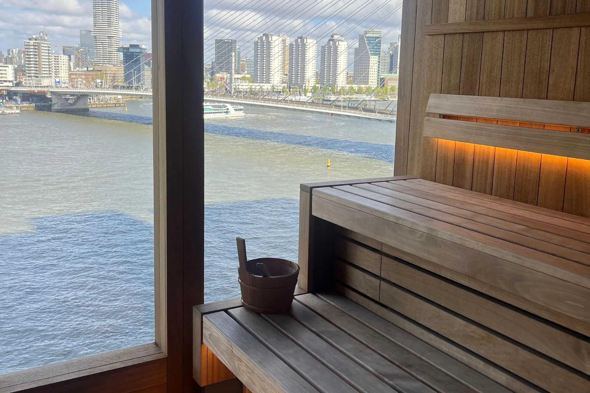 Een serene spa op de Nieuw Statendam van Holland America Line, met houten banken en een groot raam dat uitzicht biedt op de stad en een rivier.