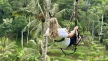 Reisadviseur Naomi schommelt boven weelderige rijstvelden in Bali, met een panoramisch uitzicht op groene natuur.