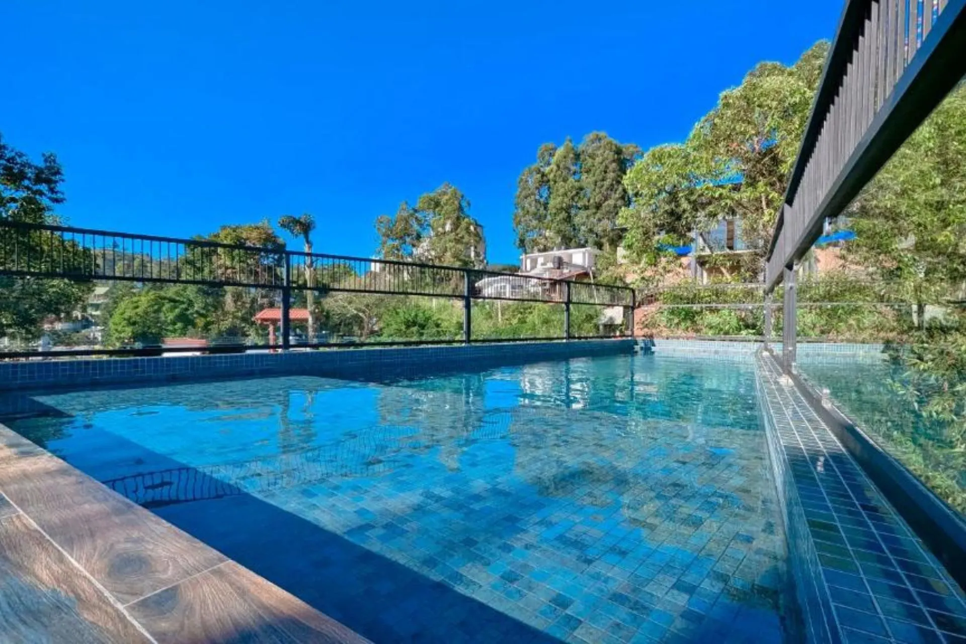 Compact zwembad van Oak Ray La Ella Breeze Hotel met glazen hek en uitzicht op de groene omgeving en beboste heuvels van Ella.