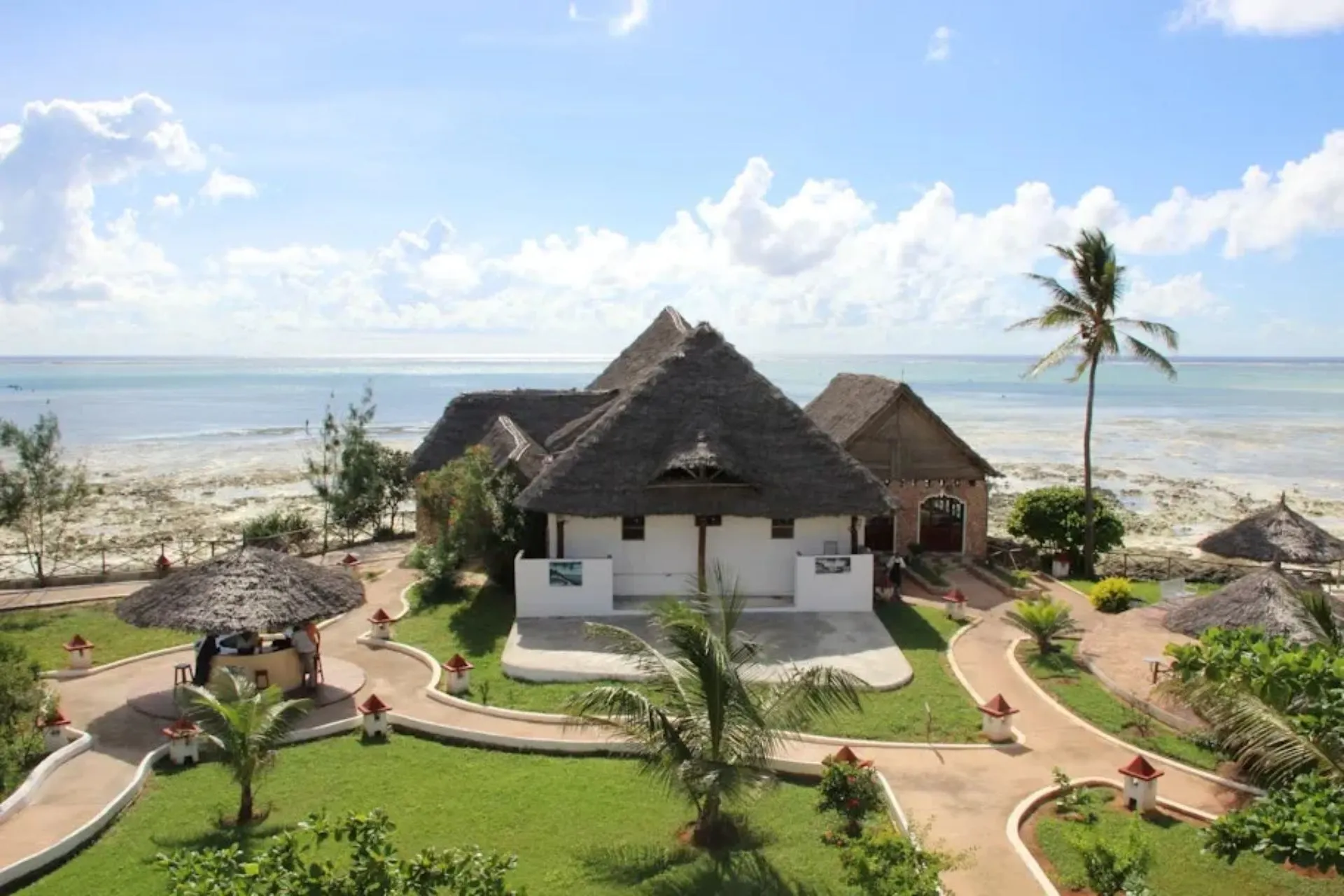 Overzicht van Reef & Beach Resort op Zanzibar, prachtig gelegen aan de kust van Jambiani. Traditionele gebouwen met rieten daken liggen midden in een tropische tuin met palmbomen en uitzicht over de Indische Oceaan. Een sfeervol resort waar strand, natuur en ontspanning samenkomen.