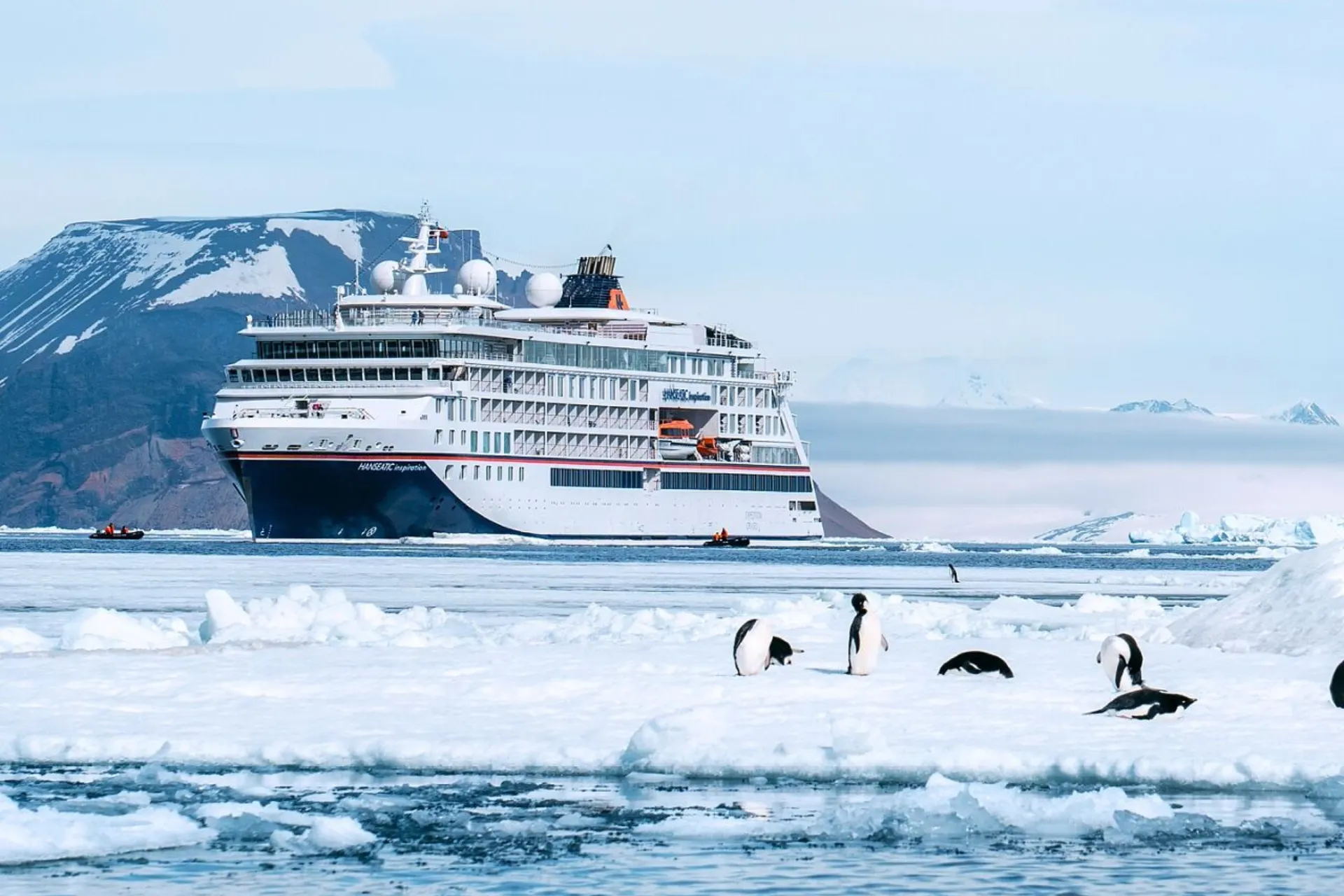 Hapag Lloyd cruiseschip voor de kust van Antarctica met pinguïns op het ijs op de voorgrond.