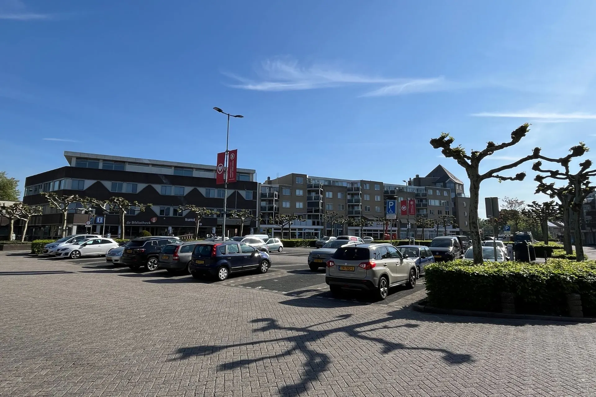 Ruime parkeerplaats aan het Mondriaanplein in Uden met zicht op de bibliotheek en winkels, dicht bij Travelcenter de Wit.