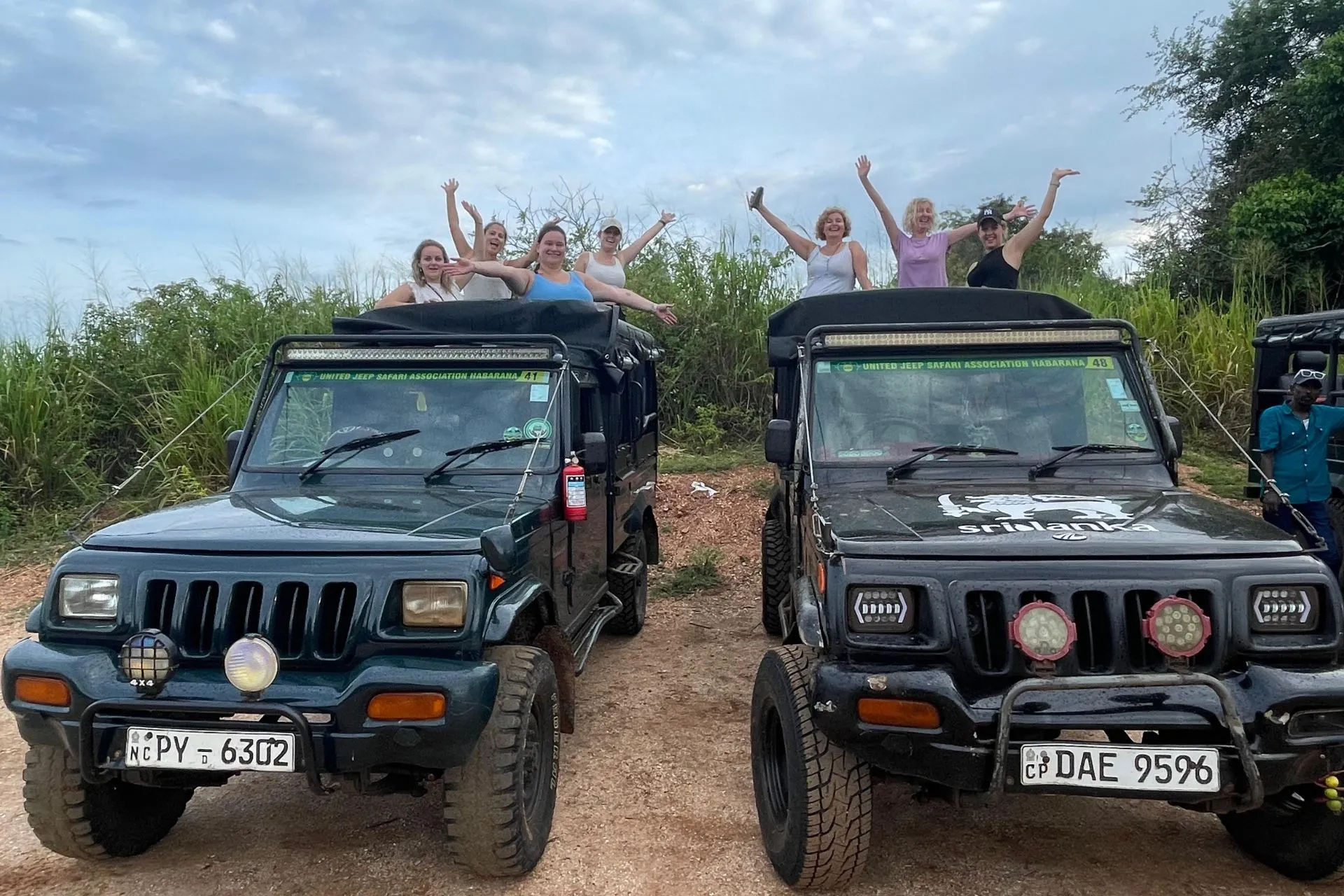 Groep enthousiaste reizigers op twee jeeps tijdens een safari in Sri Lanka, zwaaiend naar de camera bij zonsondergang.

