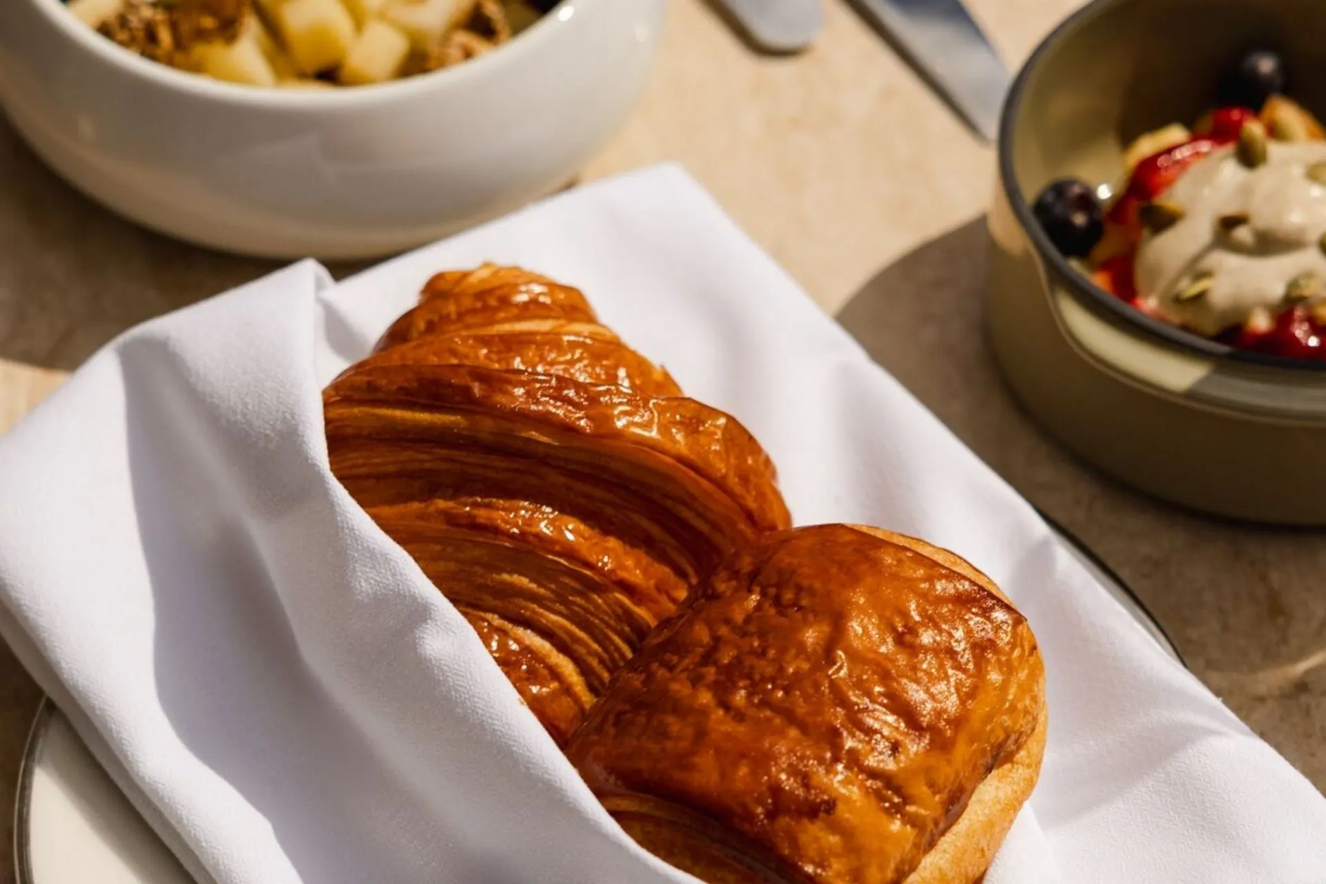 Versgebakken croissant geserveerd in een elegante setting tijdens een Explora cruise. Combineer deze Franse klassieker met gezonde opties zoals granola en fruit, onderdeel van het uitgebreide Explora dining aanbod. Ideaal voor reizigers die Explora boeken en genieten van een premium ontbijt in Explora suites aan boord van Explora I of Explora II, waar luxe en smaak centraal staan bij Explora Journeys.

