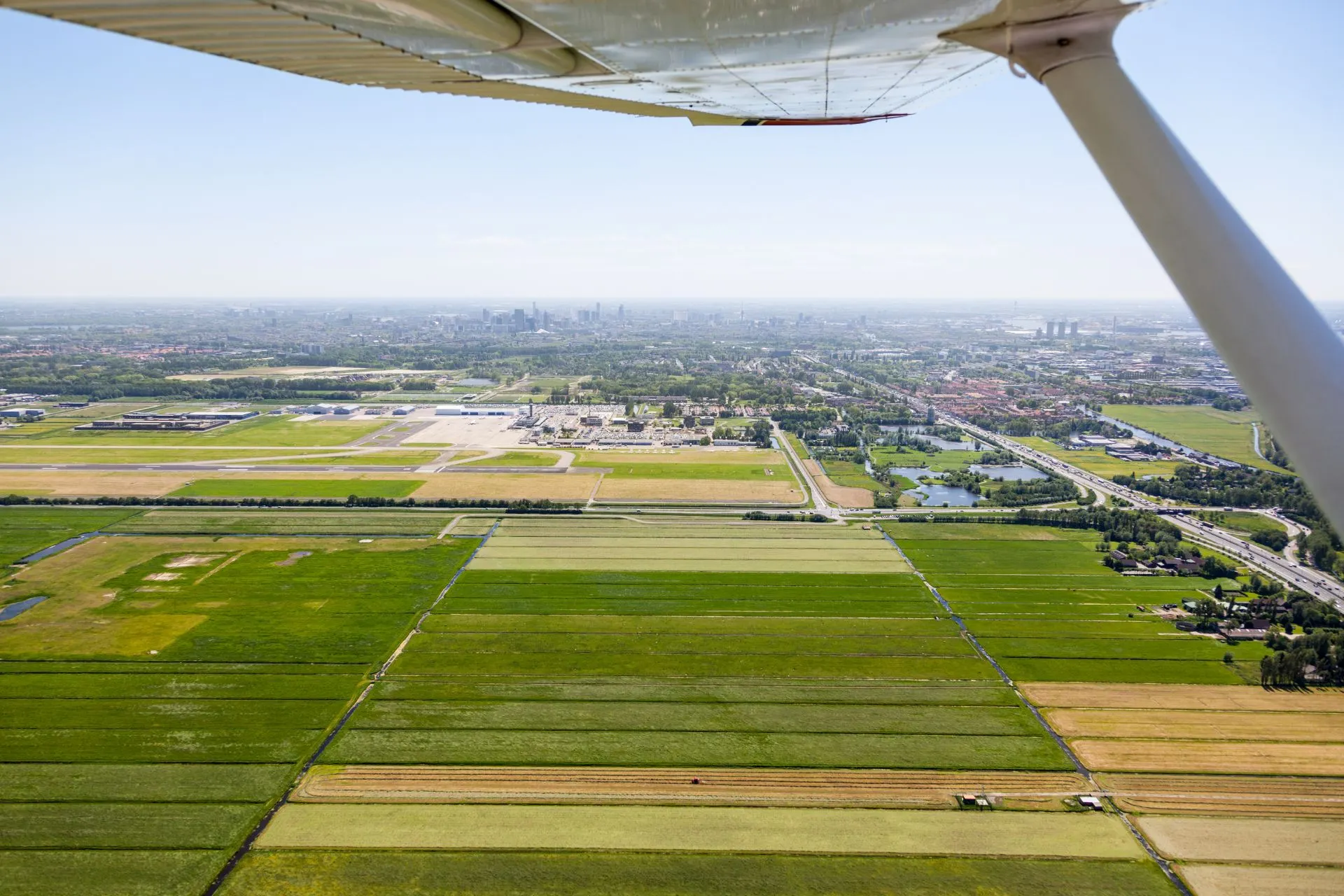 Uitzicht vanuit een vliegtuig bij vliegen vanaf Rotterdam, met groen weiland onder je. Geniet van een ontspannen start met vluchten vanaf Rotterdam Airport en ervaar het gemak van vertrek vanaf Luchthaven Rotterdam.