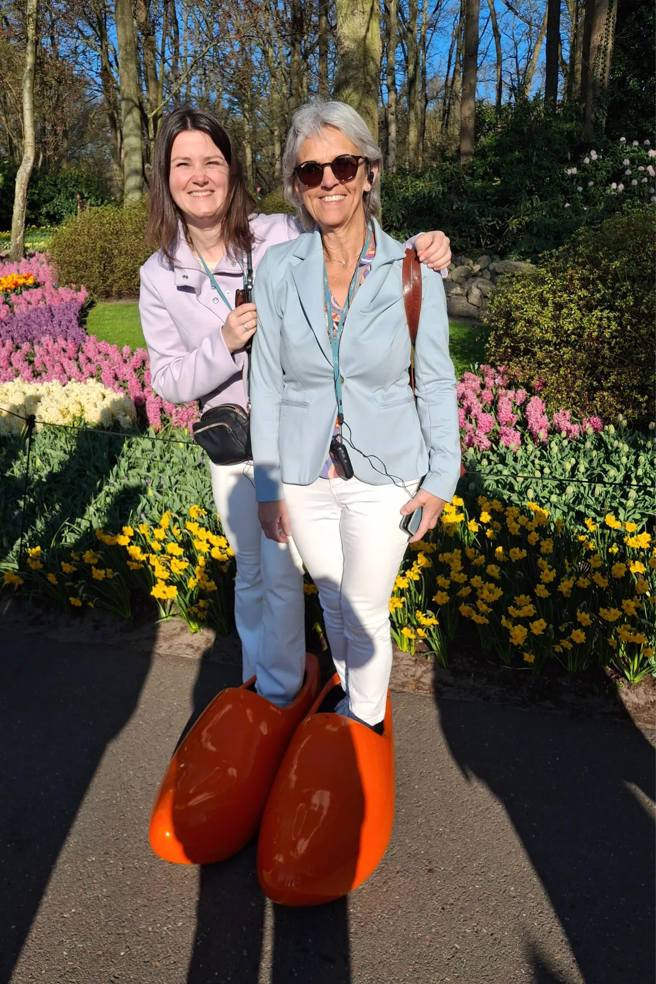 Marianne en Renée lachend samen in grote rode klompen, poserend voor een vrolijke foto.