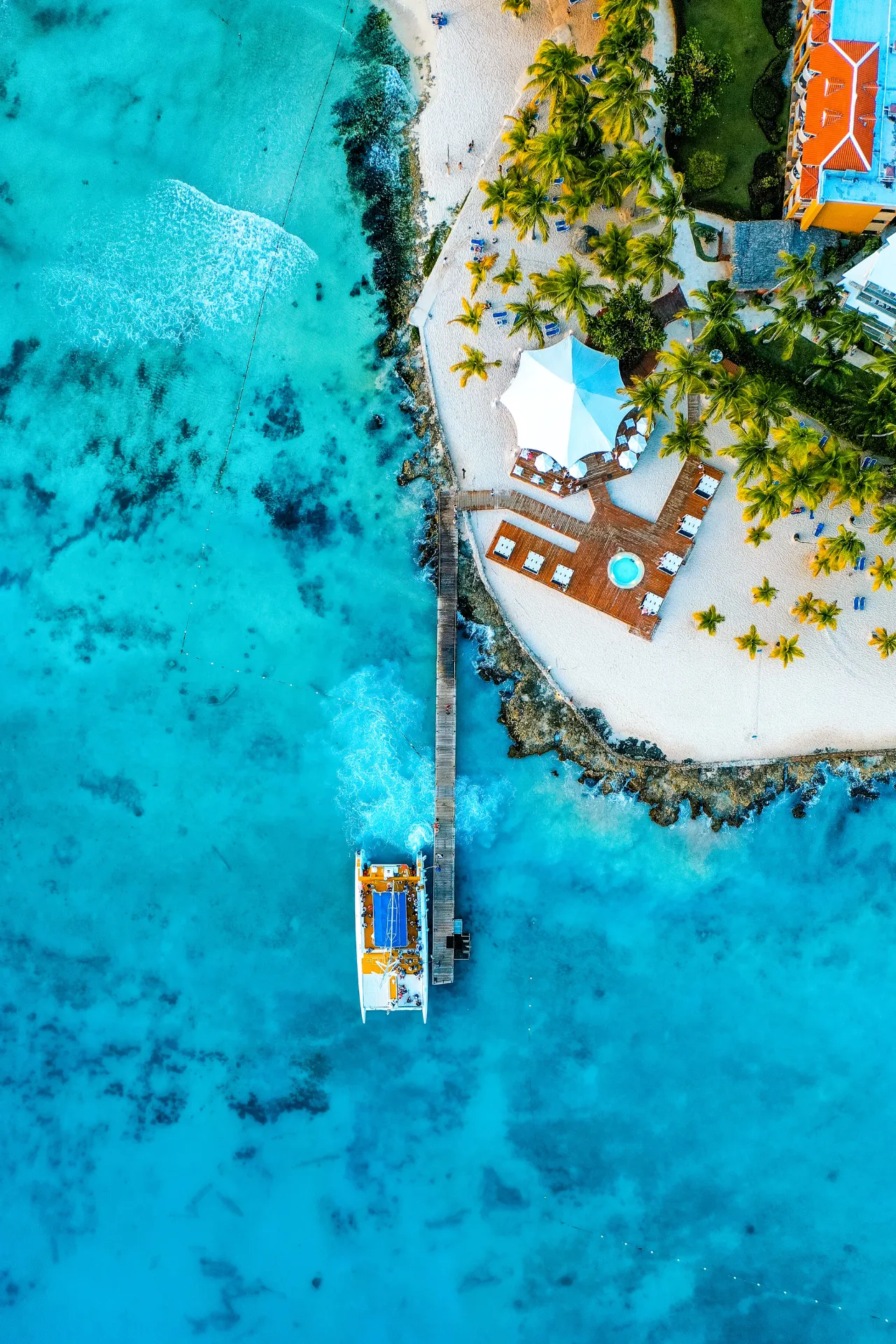 Luchtfoto van de zee bij Bayahibe in de Dominicaanse Republiek met een houten pier, een klein bootje en helderblauw water.