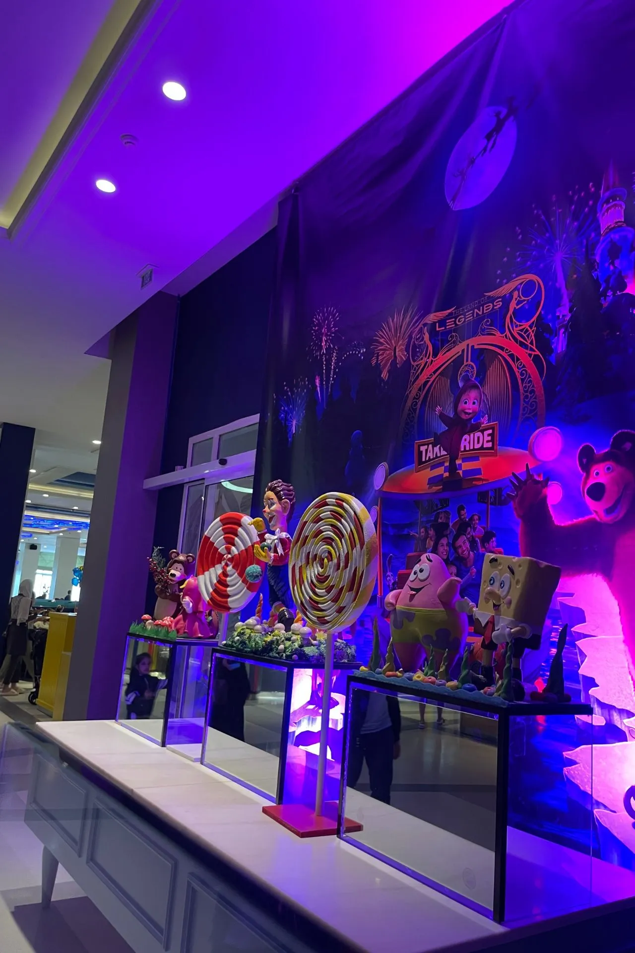 Binnenruimte met paarse verlichting en een decor van Masha en de Beer, inclusief grote lollies en kleurrijke figuren op een achtergrond vol animatie-elementen