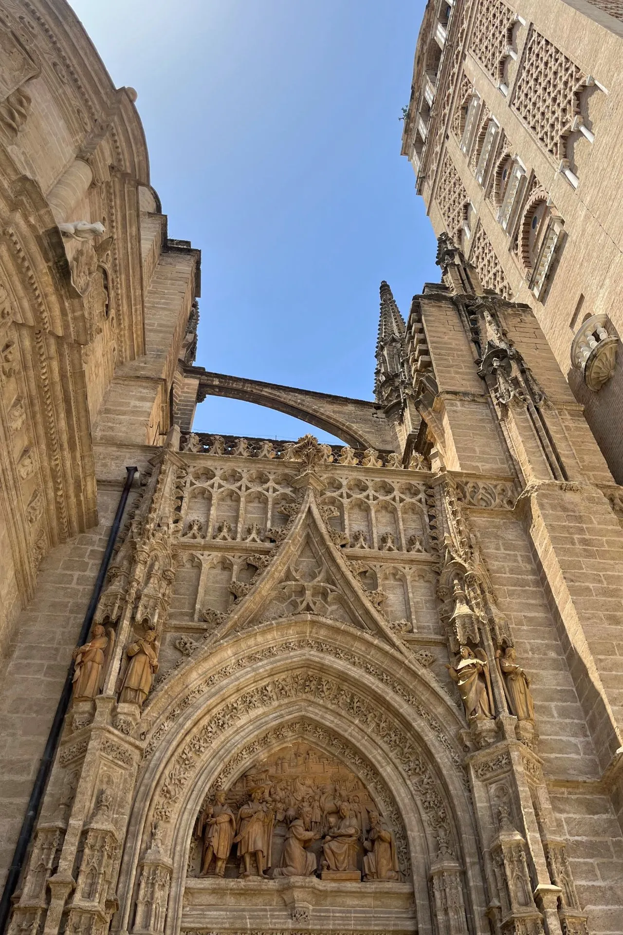 Detail van de gotische ingang van de Kathedraal van Sevilla met beeldhouwwerken en spitsbogen, gefotografeerd van onderaf naast de Giralda.