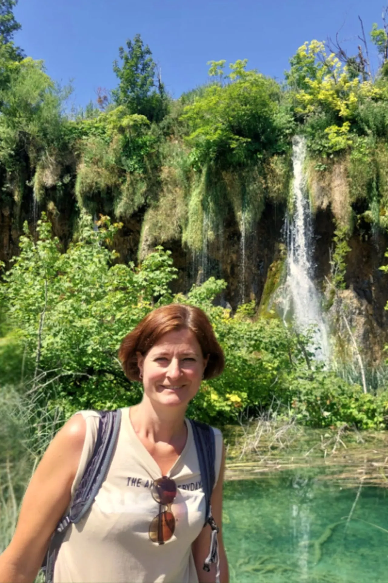 Monique poseert voor een prachtig groen landschap in het Nationaal Park Plitvice Meren, met een waterval op de achtergrond en helder turquoise water.
