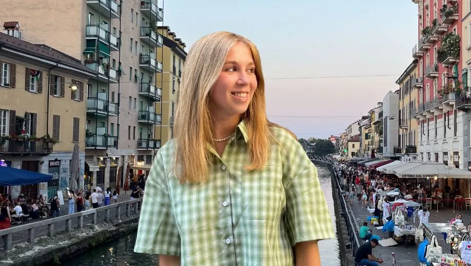 Marketeer Martje poseert lachend aan het kanaal van Navigli in Milaan, met op de achtergrond kleurrijke gebouwen, terrasjes en een levendige avondmarkt langs het water.