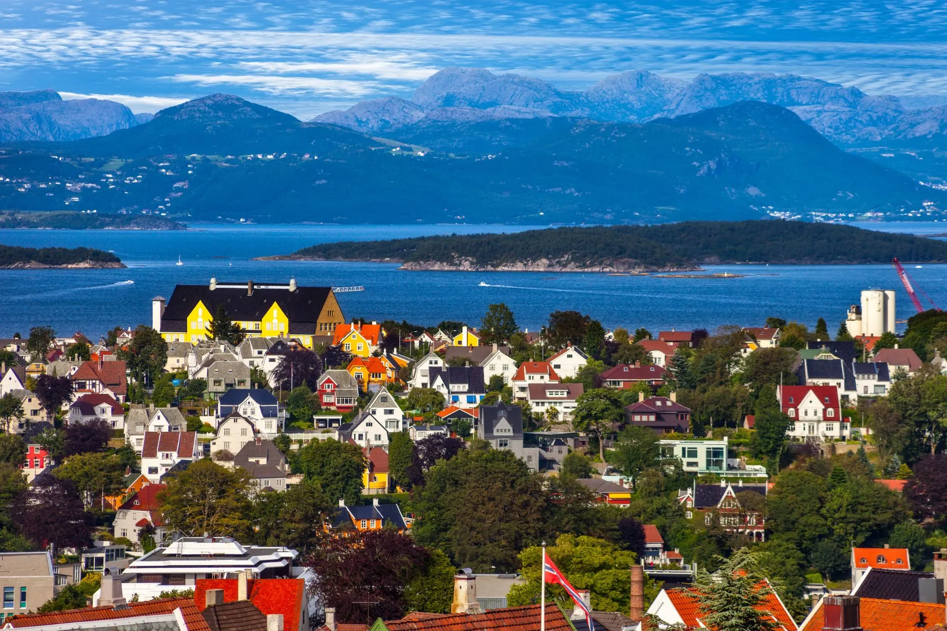 Kleurrijke huizen in Stavanger met uitzicht op het fjord en de bergen op de achtergrond, onder een deels bewolkte blauwe lucht.