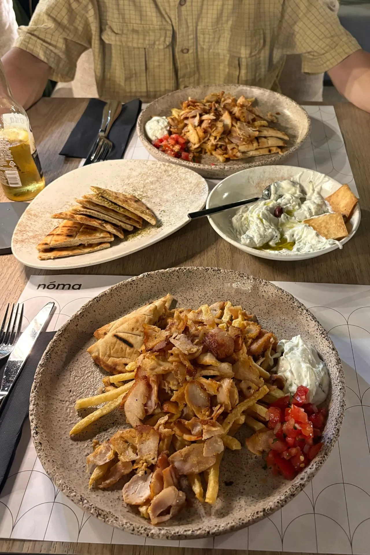 Tafel vol gyros, pita, tzatziki en friet in restaurant Nóma in Rethymnon, met moderne inrichting en gezellige sfeer.