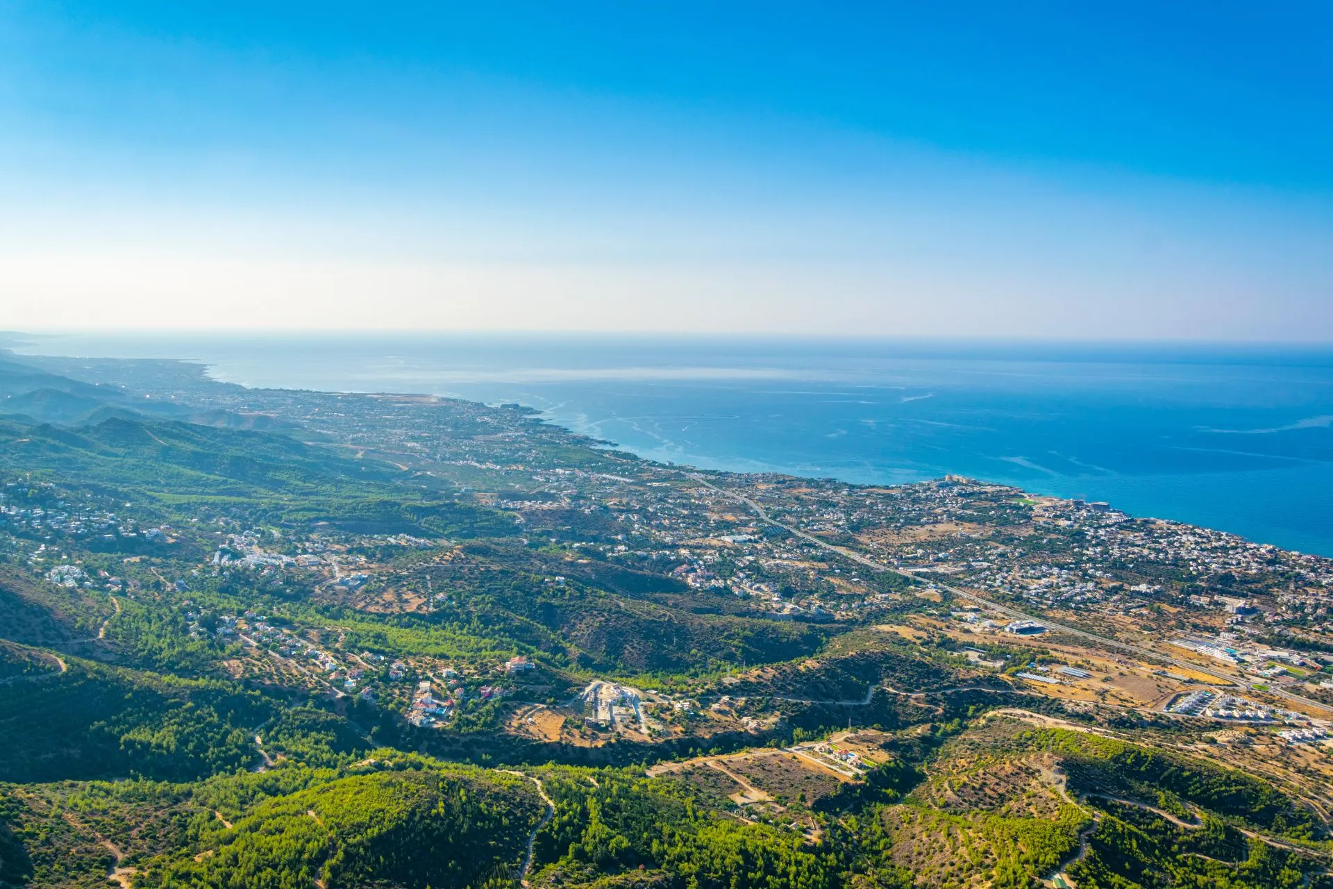 Uitgestrekt uitzicht over een zonovergoten mediterrane kustlijn met groene heuvels, kronkelende wegen en diverse dorpjes die uitkijken op helderblauw zeewater. De combinatie van natuur, heuvelachtig landschap en glinsterende kust creëert een serene en exclusieve vakantiesfeer. Dit panoramische decor sluit perfect aan bij de beleving van een luxe cruise of een all-inclusive cruise, waar reizigers genieten van comfort, vrijheid en adembenemende uitzichten tijdens een ontspannen reis langs sfeervolle kustplaatsen.