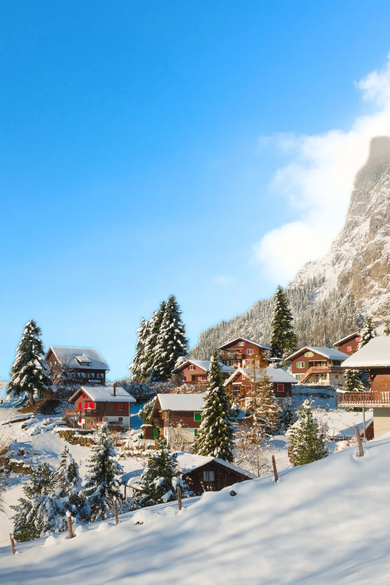 Charmante Zwitserse bergdorpjes met houten chalets, besneeuwde daken en sprookjesachtige landschappen tegen een helderblauwe lucht.