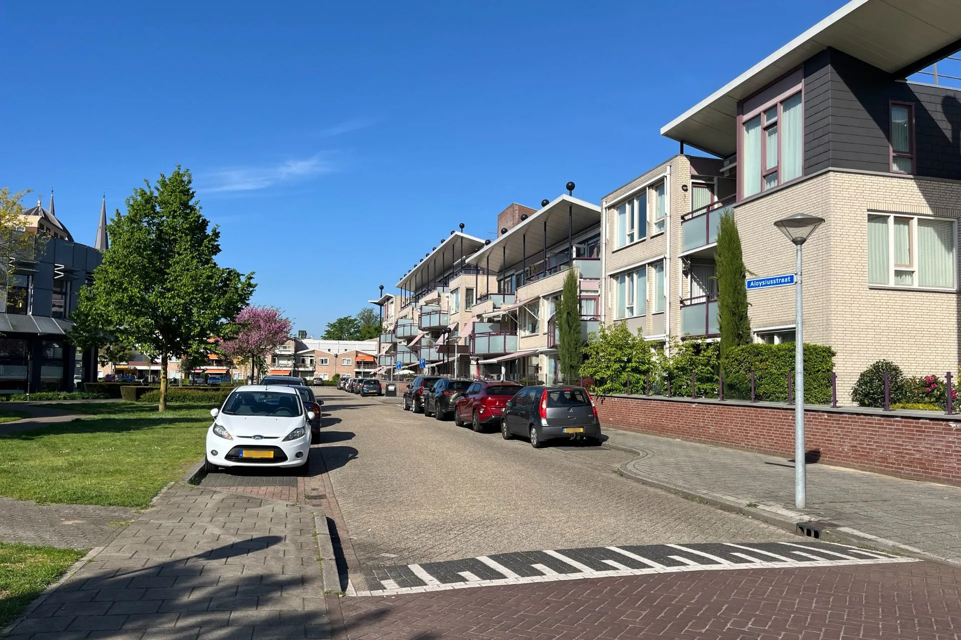 Straatbeeld van de Aloysiusstraat in Uden met parkeergelegenheden nabij Travelcenter de Wit, omringd door moderne appartementen en groenvoorzieningen.
