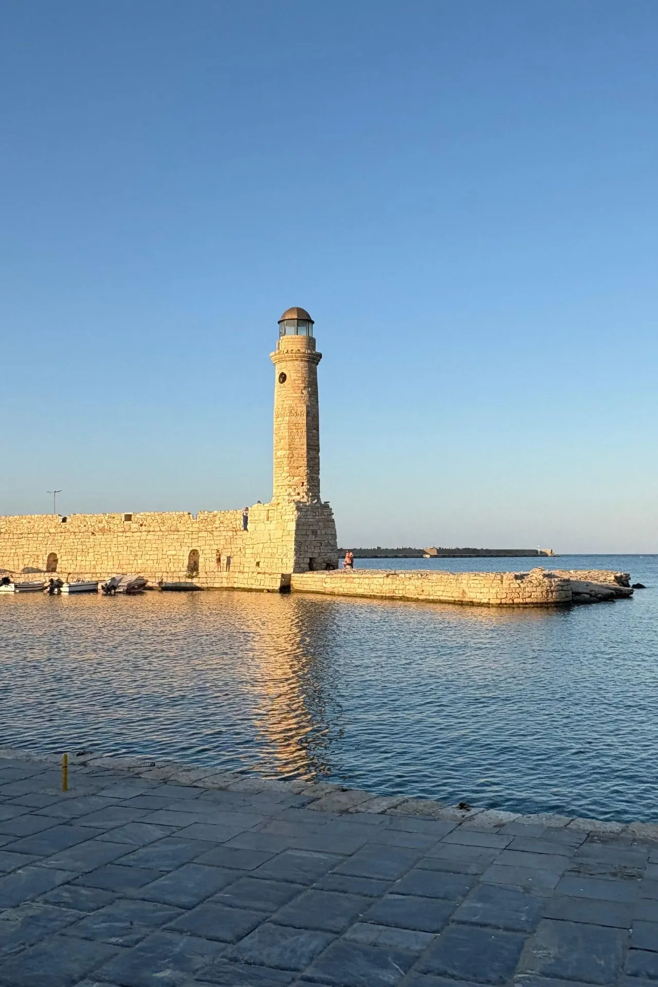 De Venetiaanse vuurtoren van Rethymnon in het warme avondlicht, weerspiegeld in het rustige water van de haven.