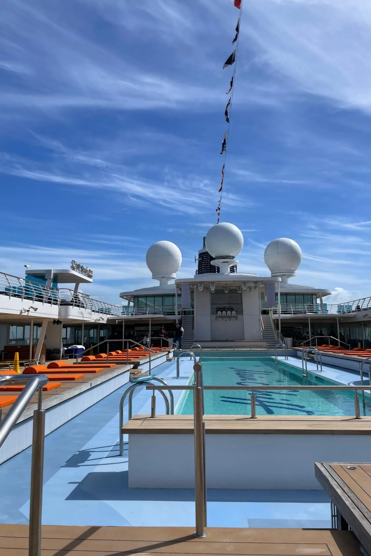Zwembad op het buitendek van Mein Schiff 3 met ligbedden en blauwe lucht tijdens een zeedag
