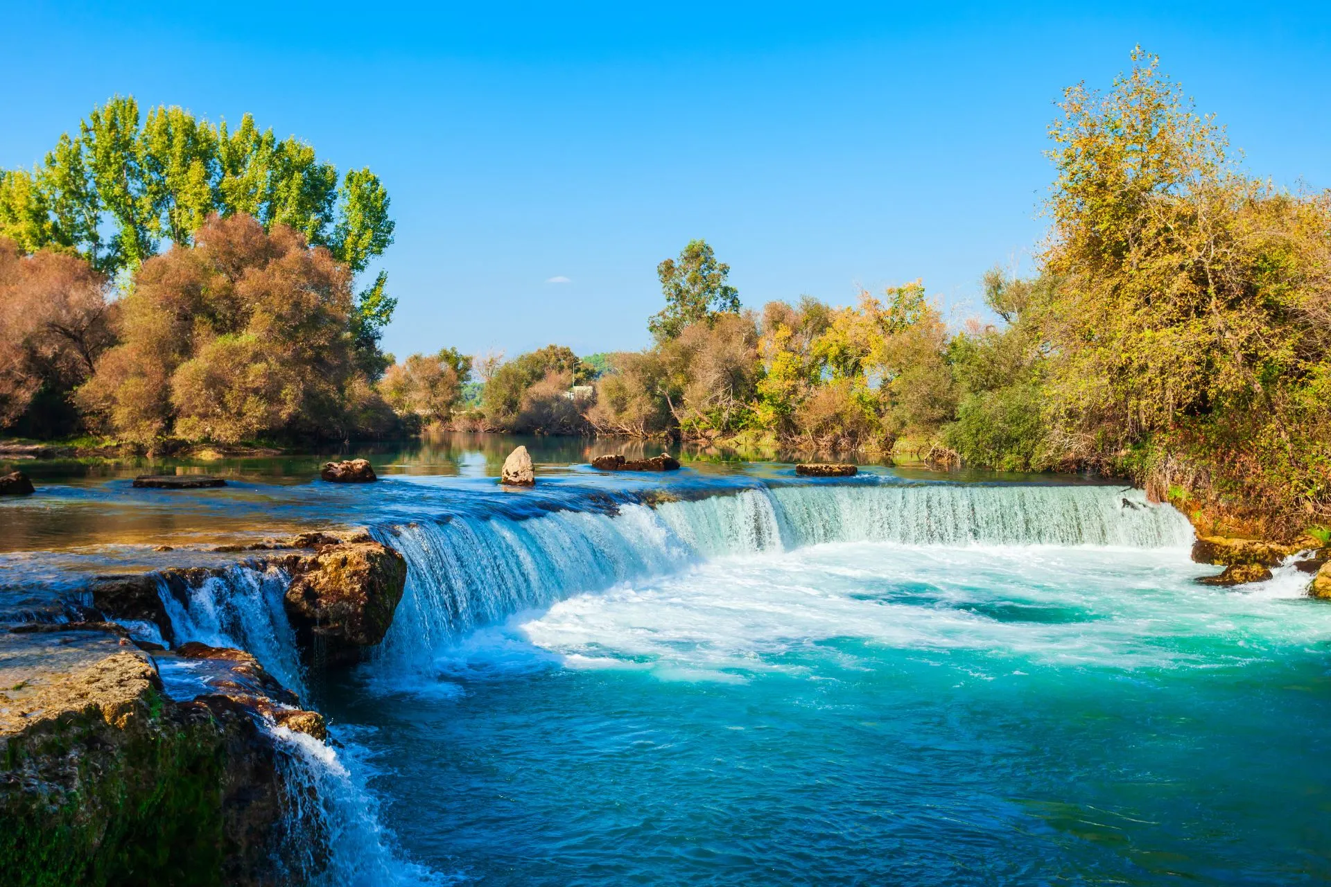 De watervallen van Manavgat in Turkije stromen krachtig over een brede rotsformatie, omringd door groene bomen en helderblauw water. Deze populaire bezienswaardigheid ligt nabij Side en is een geliefde excursie voor vakantiegangers die natuur, rust en mooie uitzichten willen combineren tijdens hun verblijf aan de Turkse Rivièra.