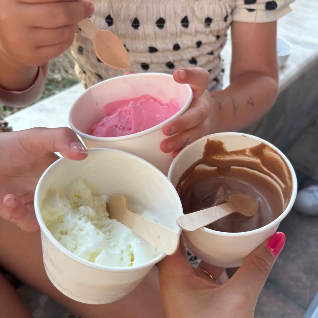 Drie handen houden bekertjes met roze, witte en bruine ijs in de lucht – een verfrissende traktatie op een warme vakantiedag in Griekenland