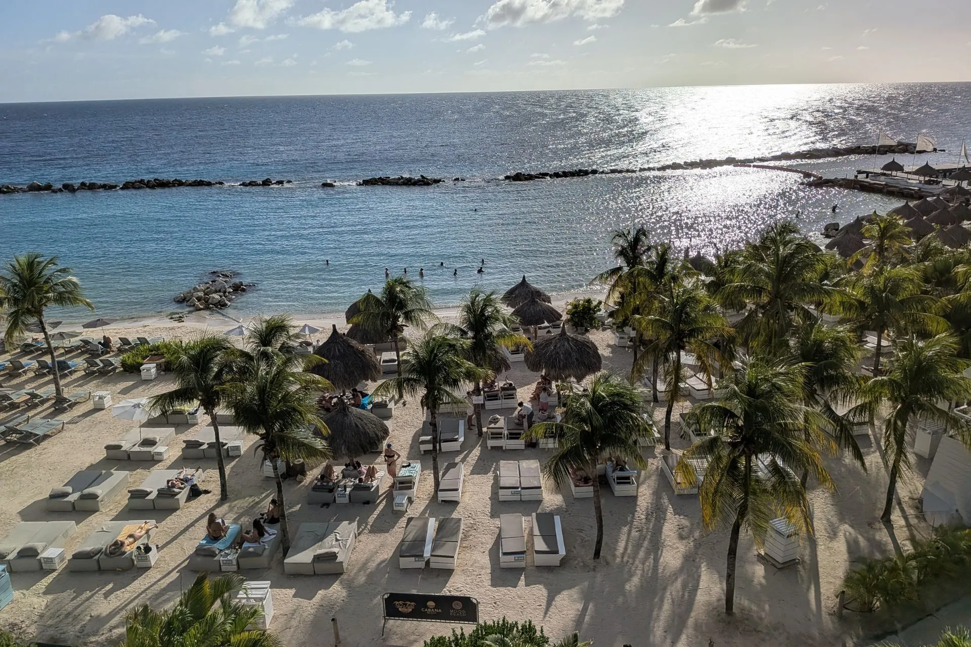 Prachtig uitzicht op een luxe strandresort op Curaçao met witte ligbedden, palmbomen en helderblauw water. De zon weerspiegelt op de zee, terwijl gasten ontspannen op het strand. Ideaal voor een zonvakantie, all-inclusive verblijf en genieten van het Caribische klimaat. Perfect voor rust, comfort en tropische vibes.