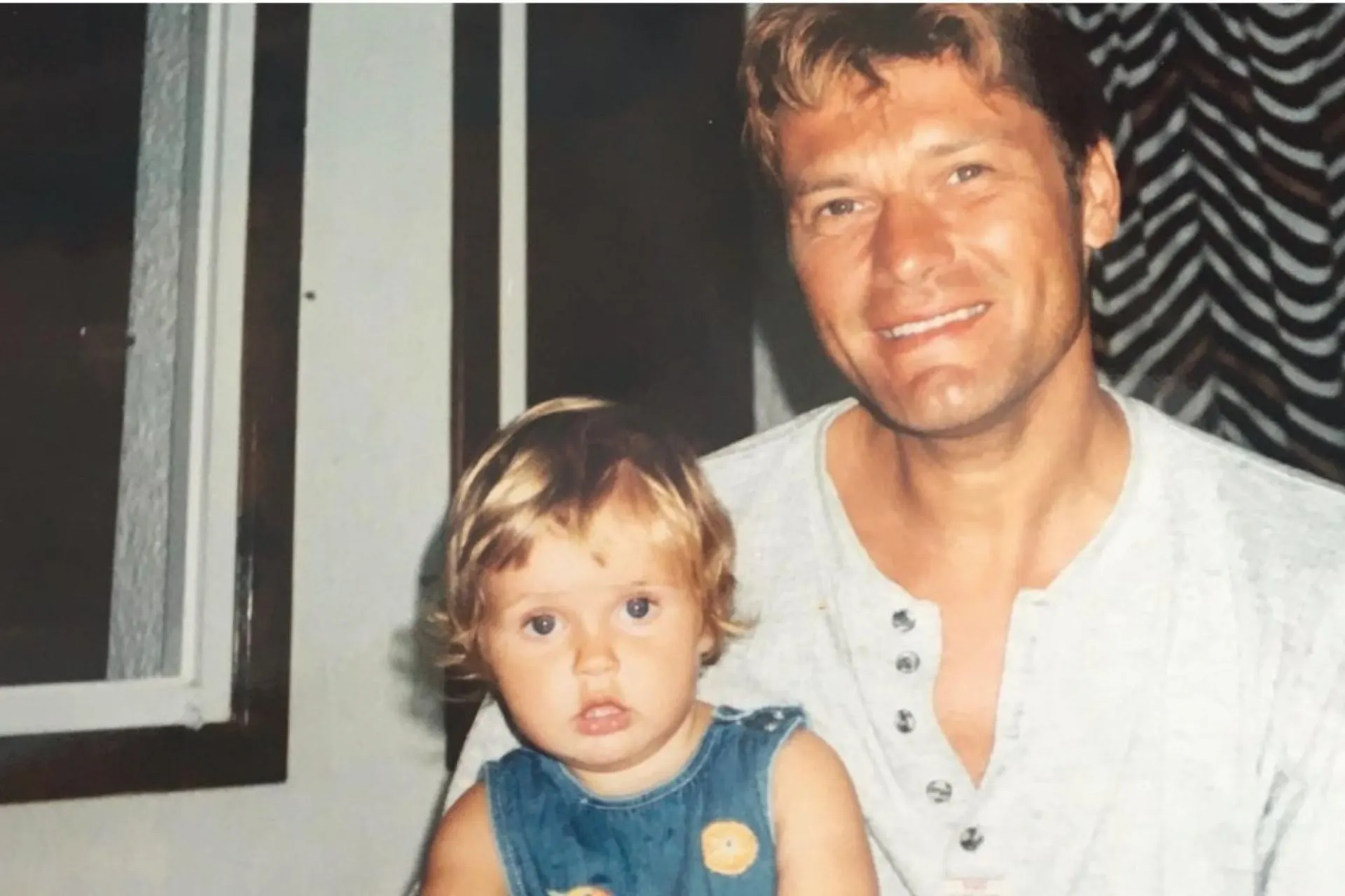 Een interieurfoto met een volwassene en een jong kind in een huiselijke omgeving, vastgelegd in een informele en persoonlijke setting. De kleding oogt casual en comfortabel, wat bijdraagt aan een warme en authentieke uitstraling. De achtergrond laat elementen van een woning zien, wat de foto geschikt maakt voor thema’s als gezin, persoonlijke levensstijl, herinneringen, familiemomenten en storytelling. Ideaal voor content over familie, welzijn, persoonlijke blogs en emotionele merkverhalen.