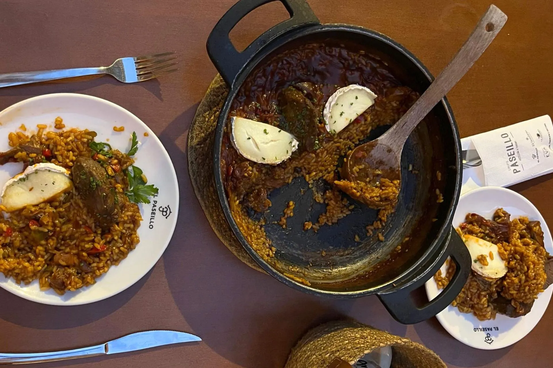 Bovenaanzicht van een pan met paella, gestoofd vlees en geitenkaas in een bruinrode saus, geserveerd bij El Paseillo in Sevilla. Er liggen al porties op twee borden, klaar om opgegeten te worden.