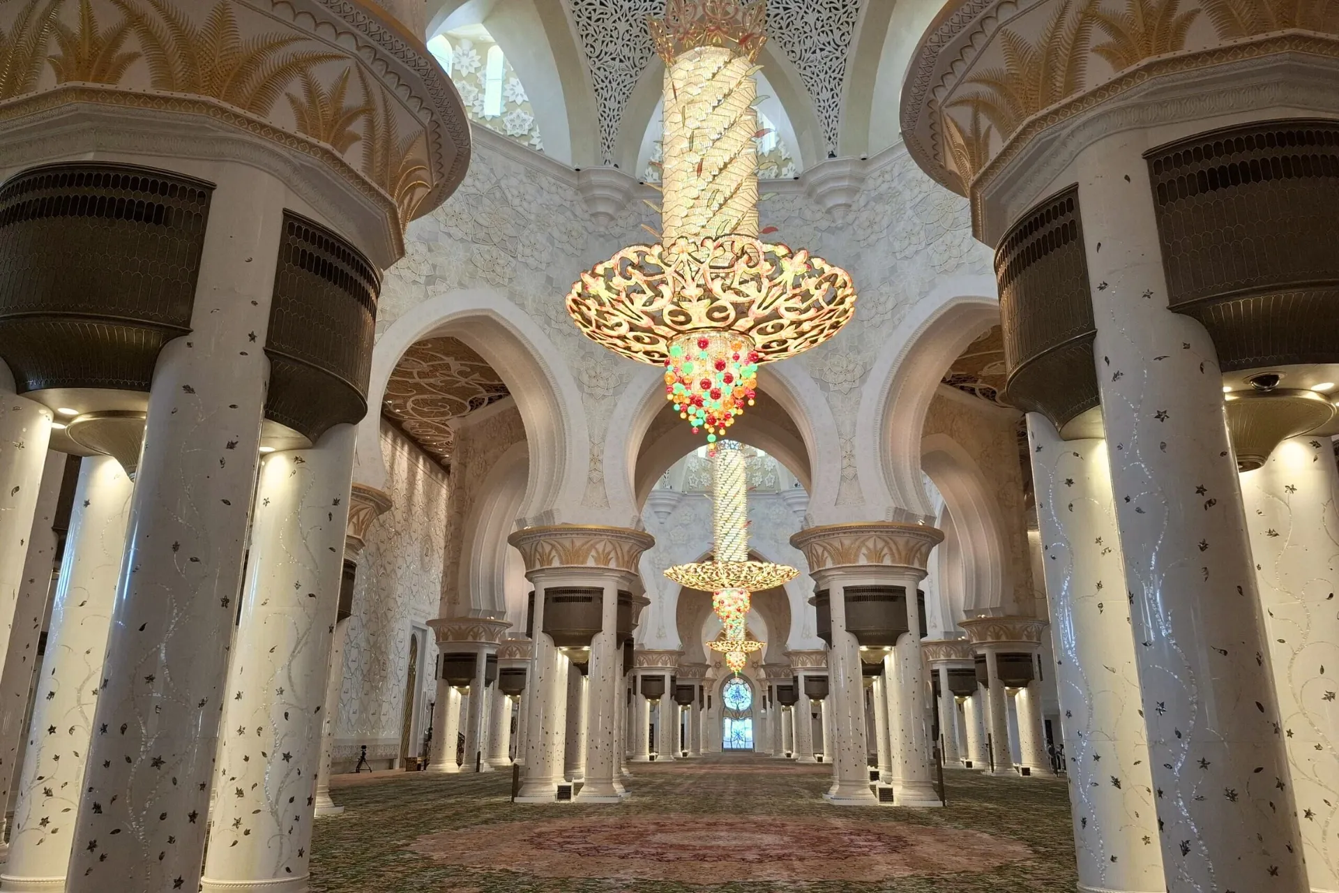 Binnenin de Sjeikh Zayed Moskee in Abu Dhabi, met het grote, witte interieur en een indrukwekkende kleurrijke lamp in het midden.
