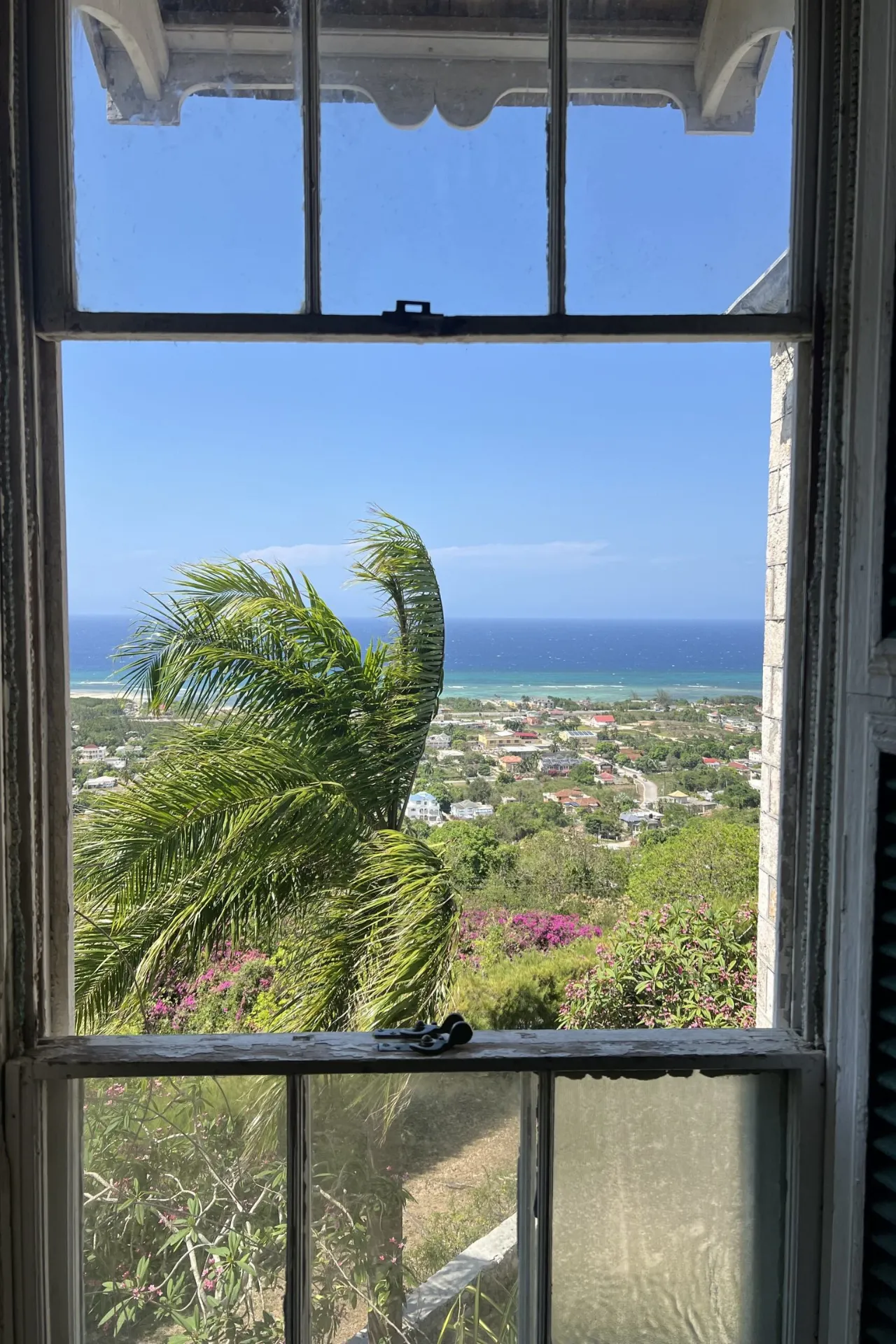 Uitzicht vanuit een raam van Greenwood Great House in Jamaica, met uitzicht op het uitgestrekte landschap en de zee aan de horizon.