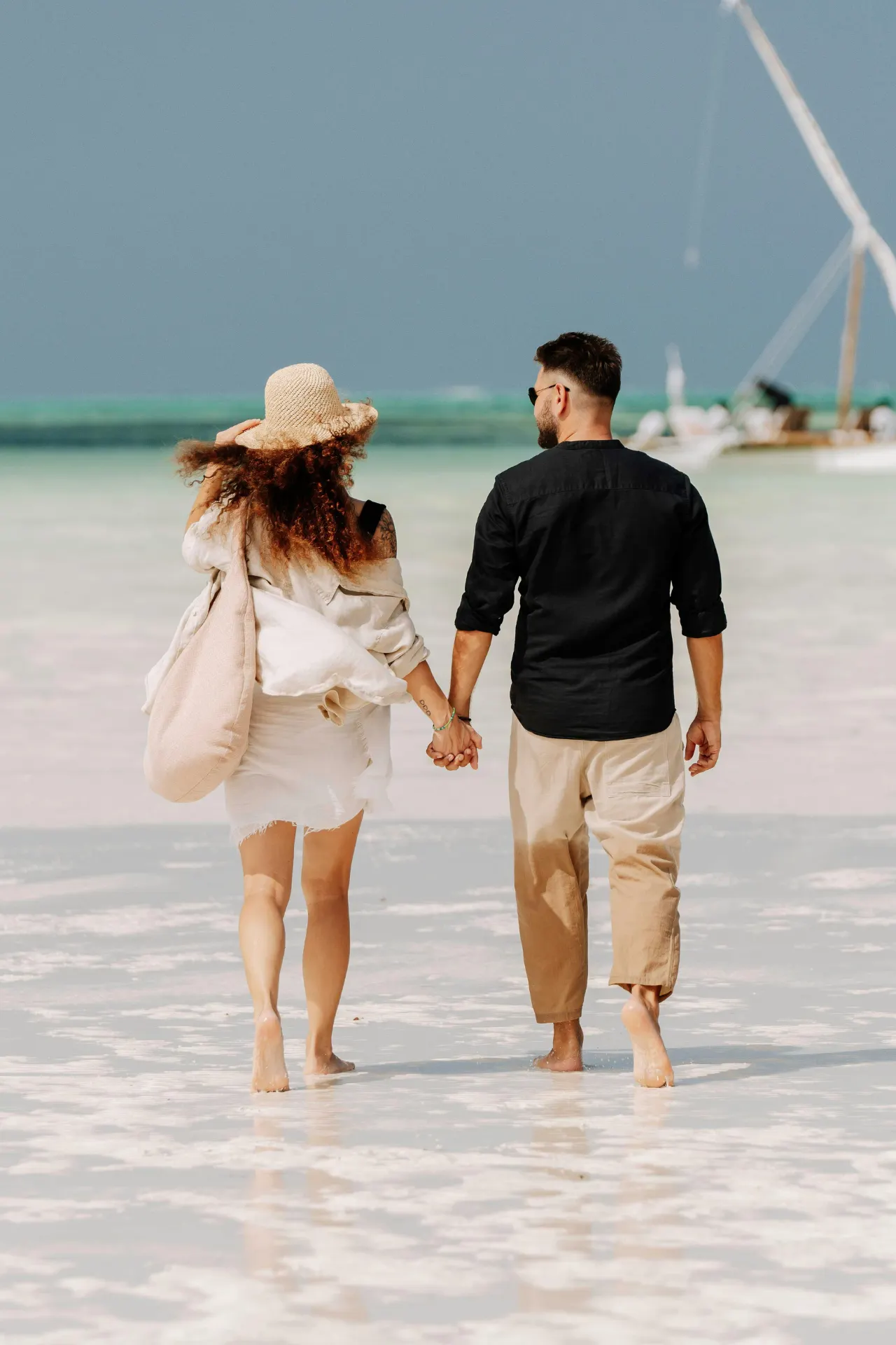 Koppel wandelt hand in hand over het witte zandstrand op Zanzibar.