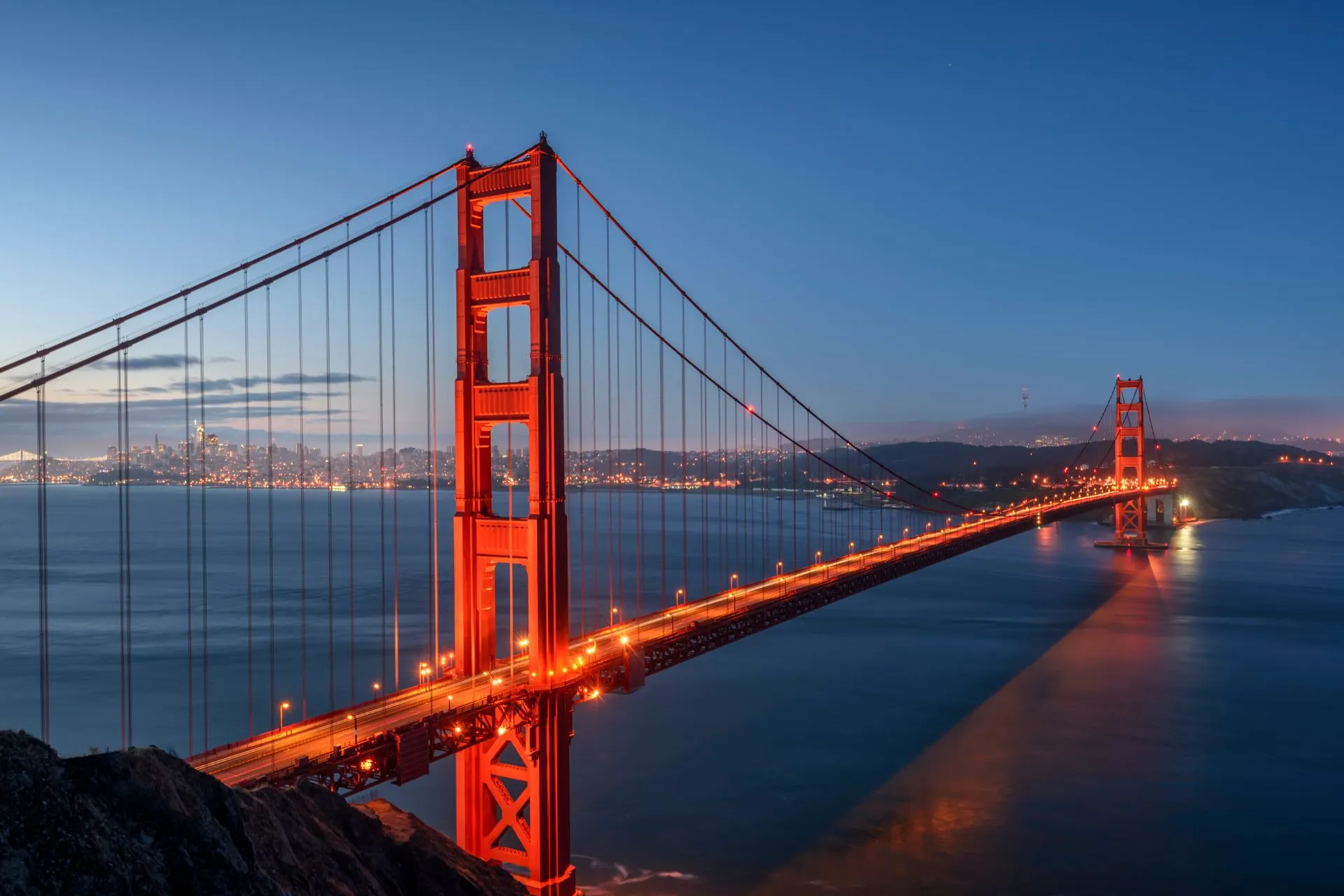 Golden Gate Bridge in San Francisco bij schemering met stadslicht en reflecties in het water – iconisch Amerikaans uitzicht.