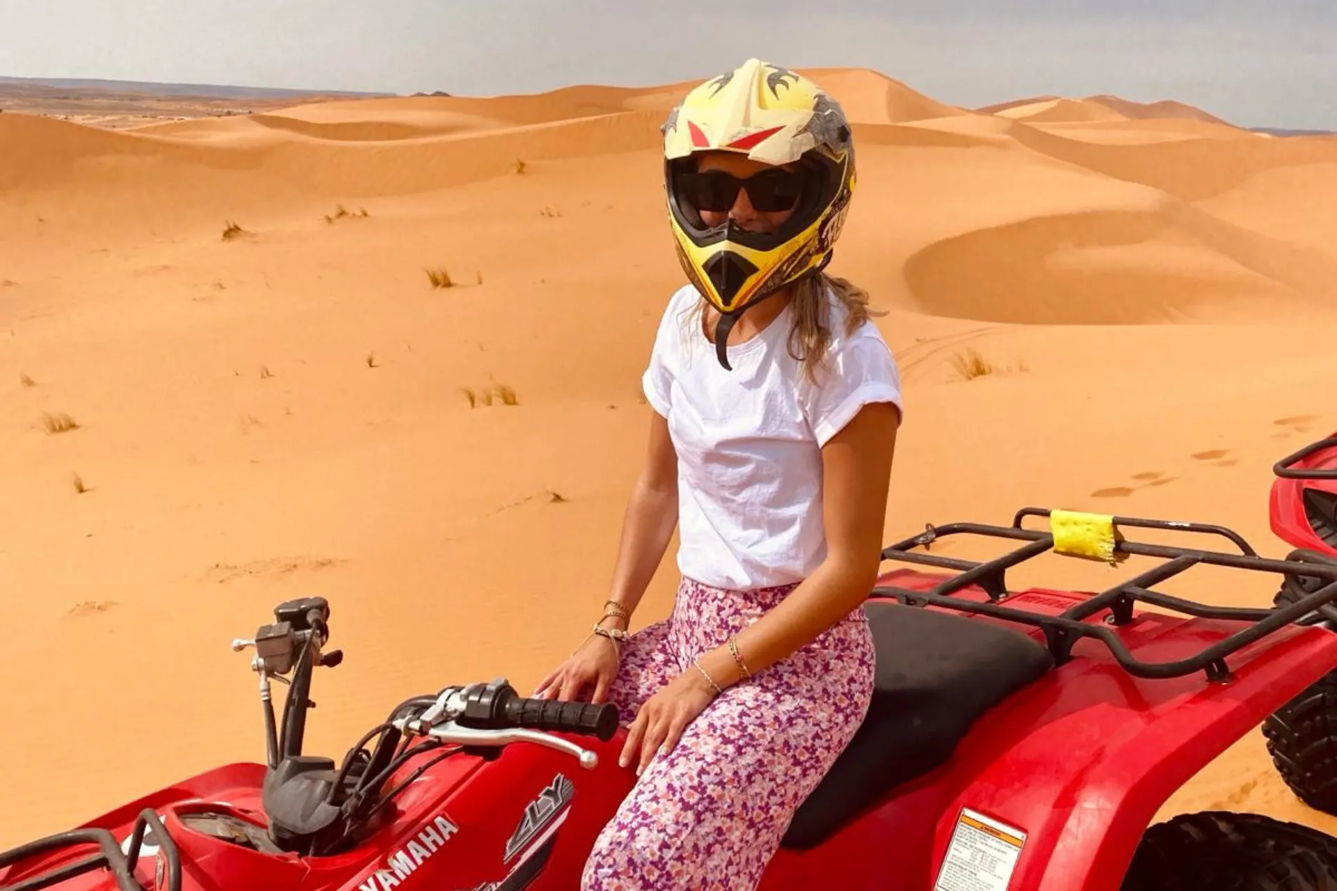  Floor rijdt op een quad door de uitgestrekte zandduinen van de Sahara in Marokko, met een gouden woestijnlandschap op de achtergrond.