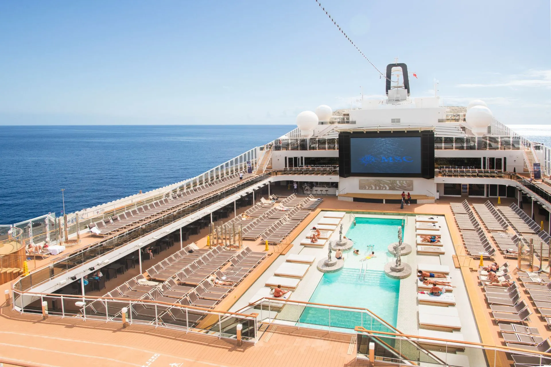 Zwembaddek van de MSC Meraviglia met ligbedden, zwembad en uitzicht op zee tijdens een cruise met MSC Cruises