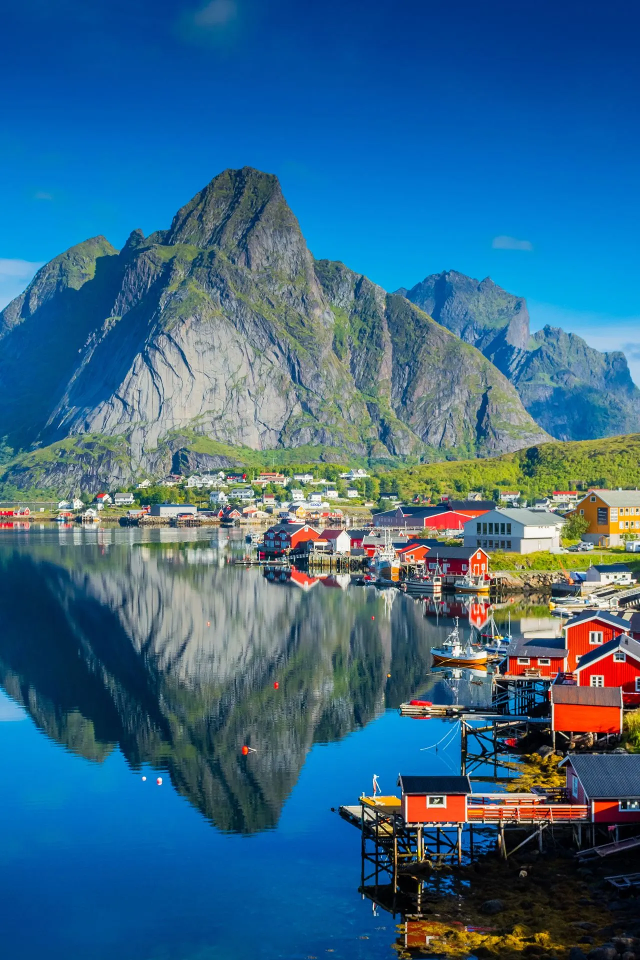 Prachtige rode vissershuisjes langs het water in de Lofoten, Noorwegen, met imposante bergen die weerspiegelen in het heldere fjord.