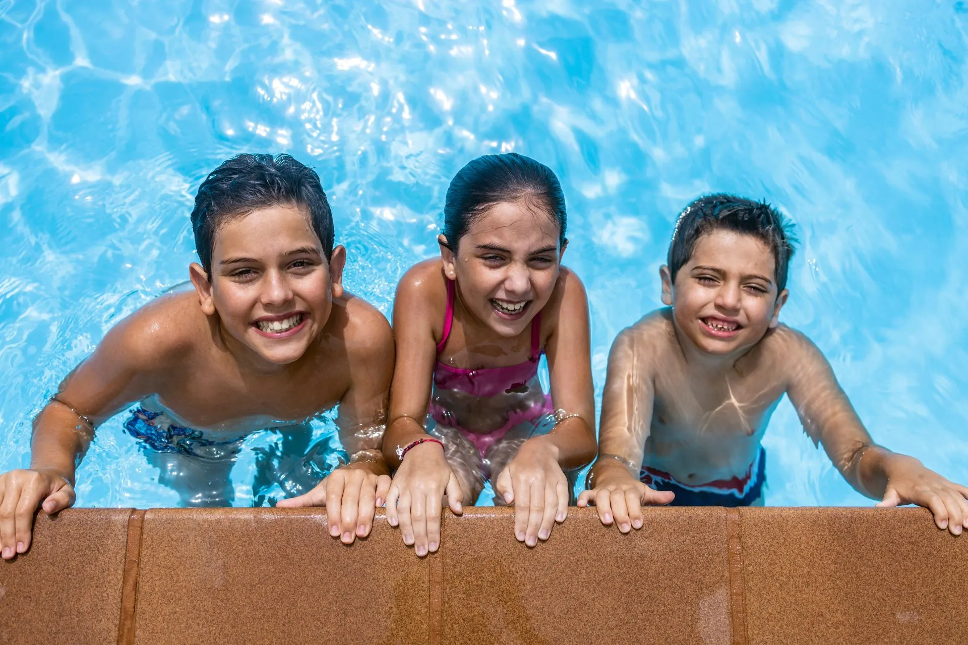 Drie kinderen genieten samen van het zwembad en houden zich vast aan de rand, omringd door helderblauw water. Deze kindvriendelijke all-inclusive bestemming biedt volop mogelijkheden voor plezier en ontspanning. Ideaal voor gezinnen die een vakantie zoeken waar kinderen veilig kunnen spelen en ouders kunnen genieten van comfort en gemak.