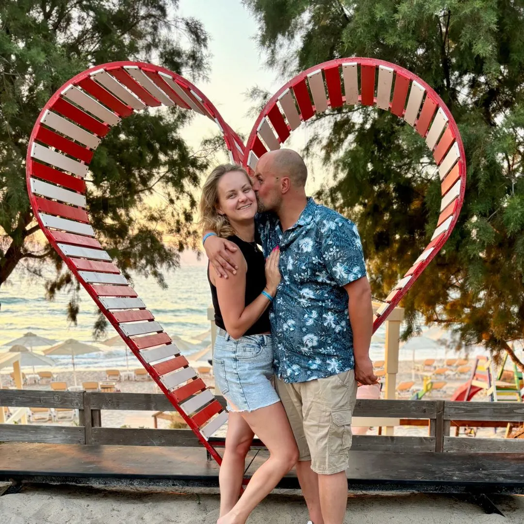 Stel geniet van een liefdevol moment bij zonsondergang op het strand van Kos, met een hartvormige fotospot en uitzicht op zee