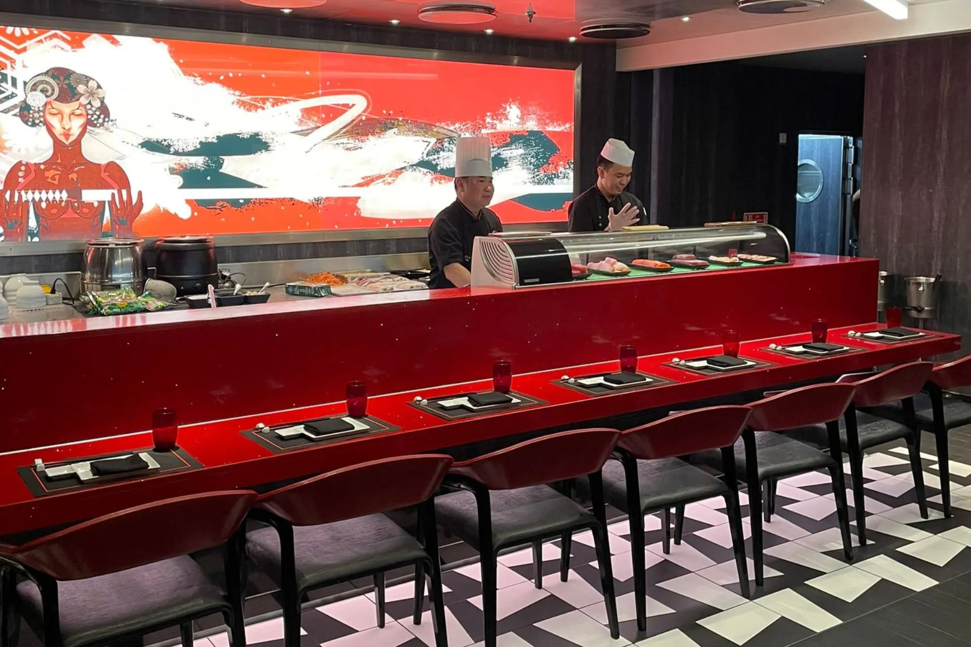 Aziatisch restaurant aan boord van de Independence of the Seas, met een rode sushibar, twee chefs in uniform en een moderne muurschildering op de achtergrond.